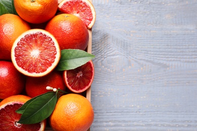 Photo of Crate of ripe red oranges and green leaves on grey wooden table, top view. Space for text