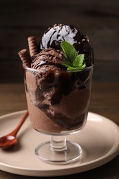 Photo of Delicious chocolate ice cream with wafer sticks, donut and mint in glass dessert bowl on table, closeup