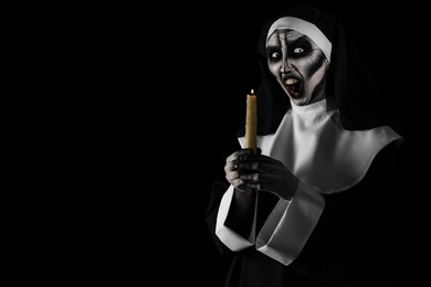 Photo of Scary devilish nun with burning candle on black background, space for text. Halloween party look