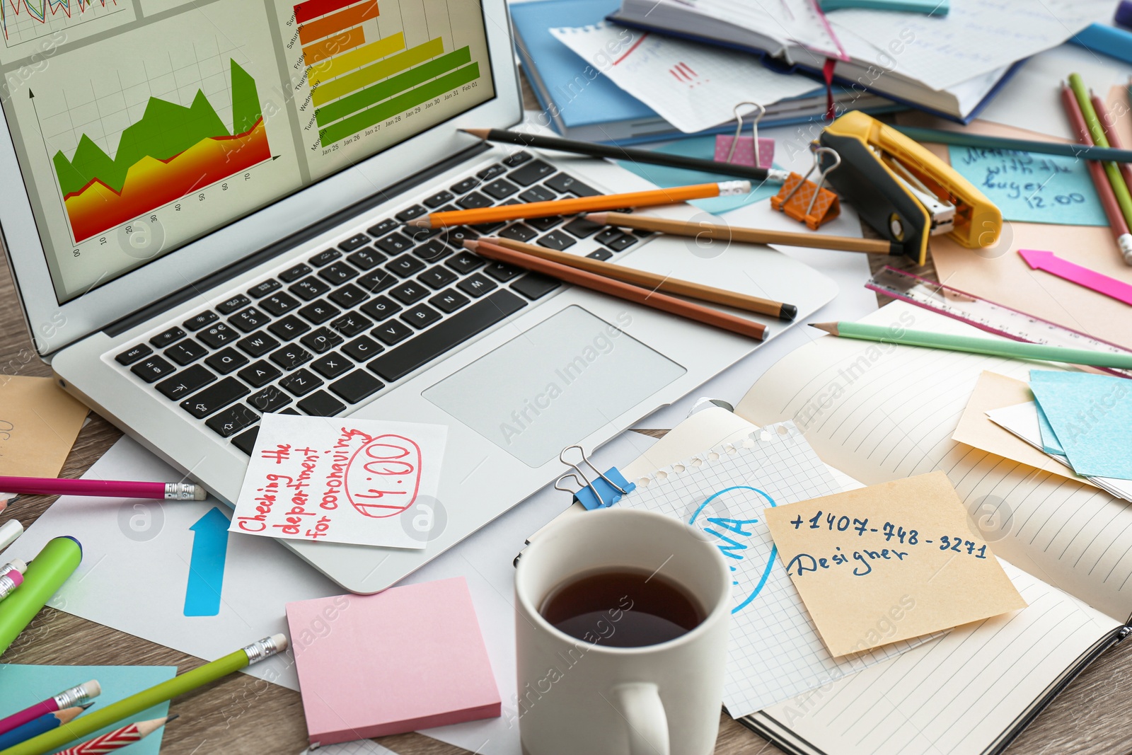 Photo of Laptop, notes and office stationery in mess on desk. Overwhelmed with work