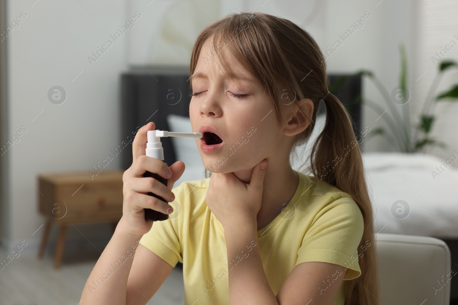 Photo of Little girl using throat spray at home