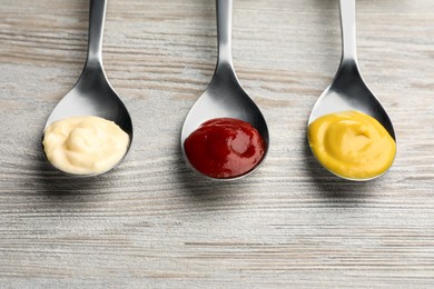 Photo of Spoons with mustard, ketchup and mayonnaise on wooden table