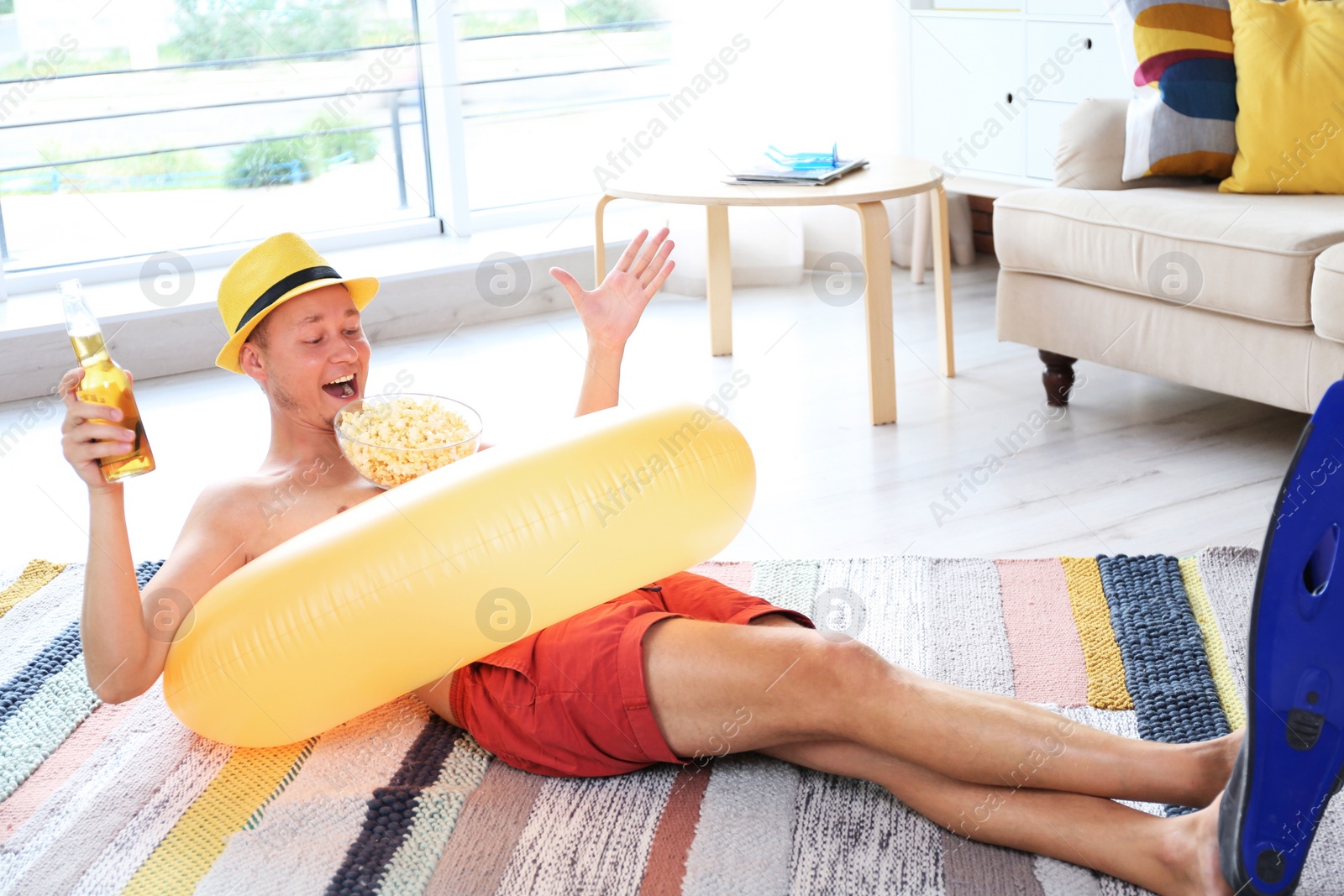 Photo of Shirtless man with inflatable ring, drink and popcorn wearing flippers on floor at home