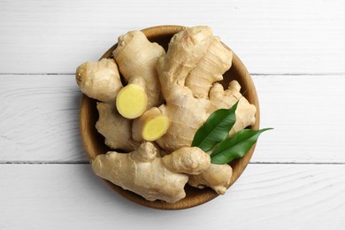 Fresh ginger with leaves in bowl on white wooden table, top view