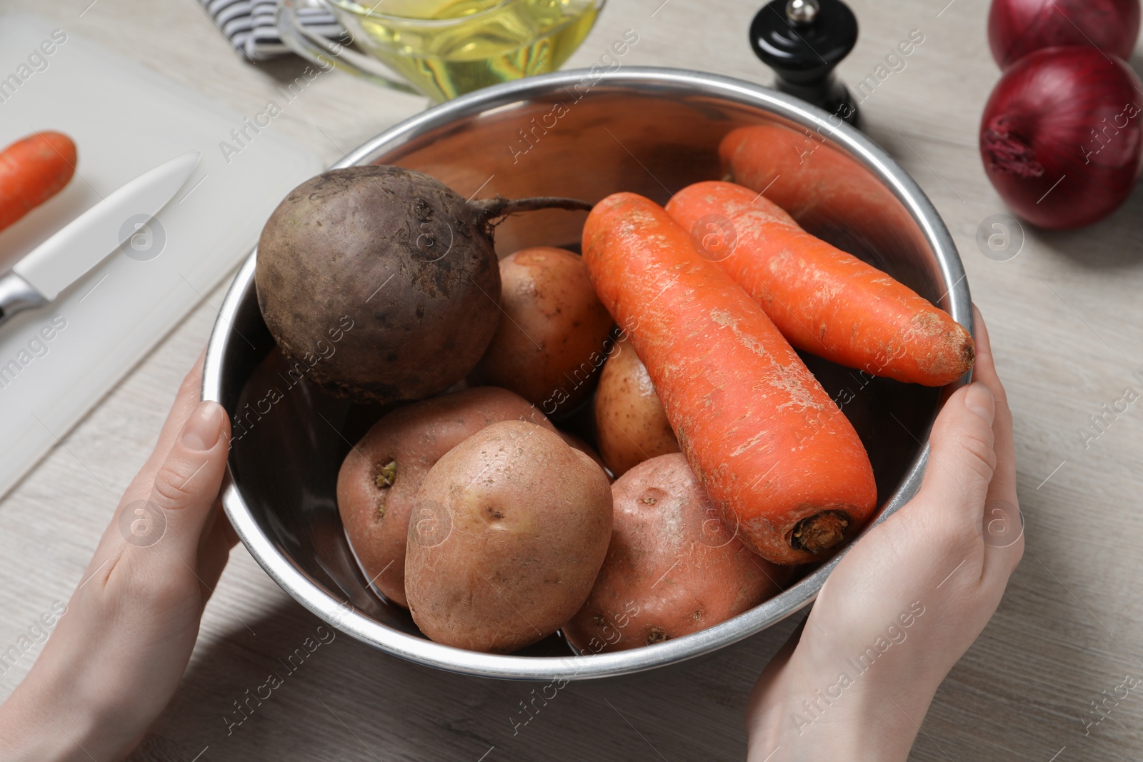 Photo of Woman with bowl of fresh vegetables at white wooden table, closeup. Cooking vinaigrette salad