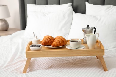 Photo of Wooden tray with tasty breakfast on bed at home