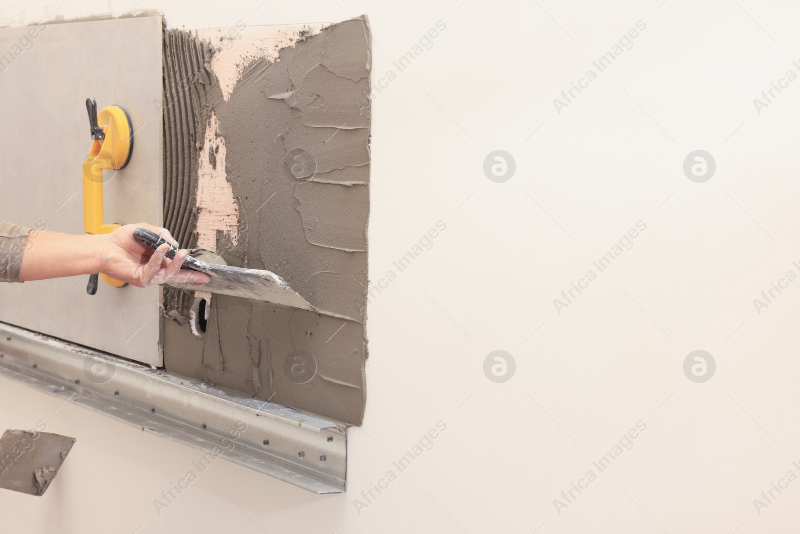 Photo of Worker spreading adhesive mix on wall for tile installation indoors, closeup