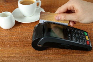 Woman with credit card using modern payment terminal at wooden table, closeup