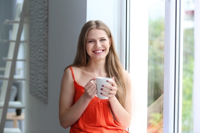 Photo of Young beautiful woman drinking morning coffee near window at home