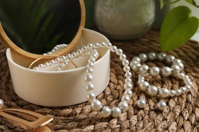 Photo of Stylish jewelry with pearls and box on wicker mat, closeup