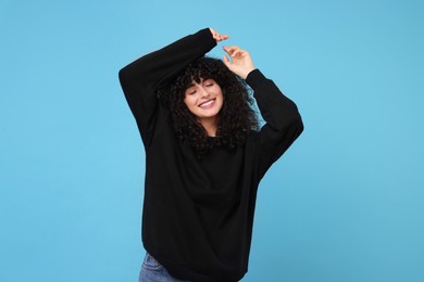 Happy young woman in stylish black sweater on light blue background