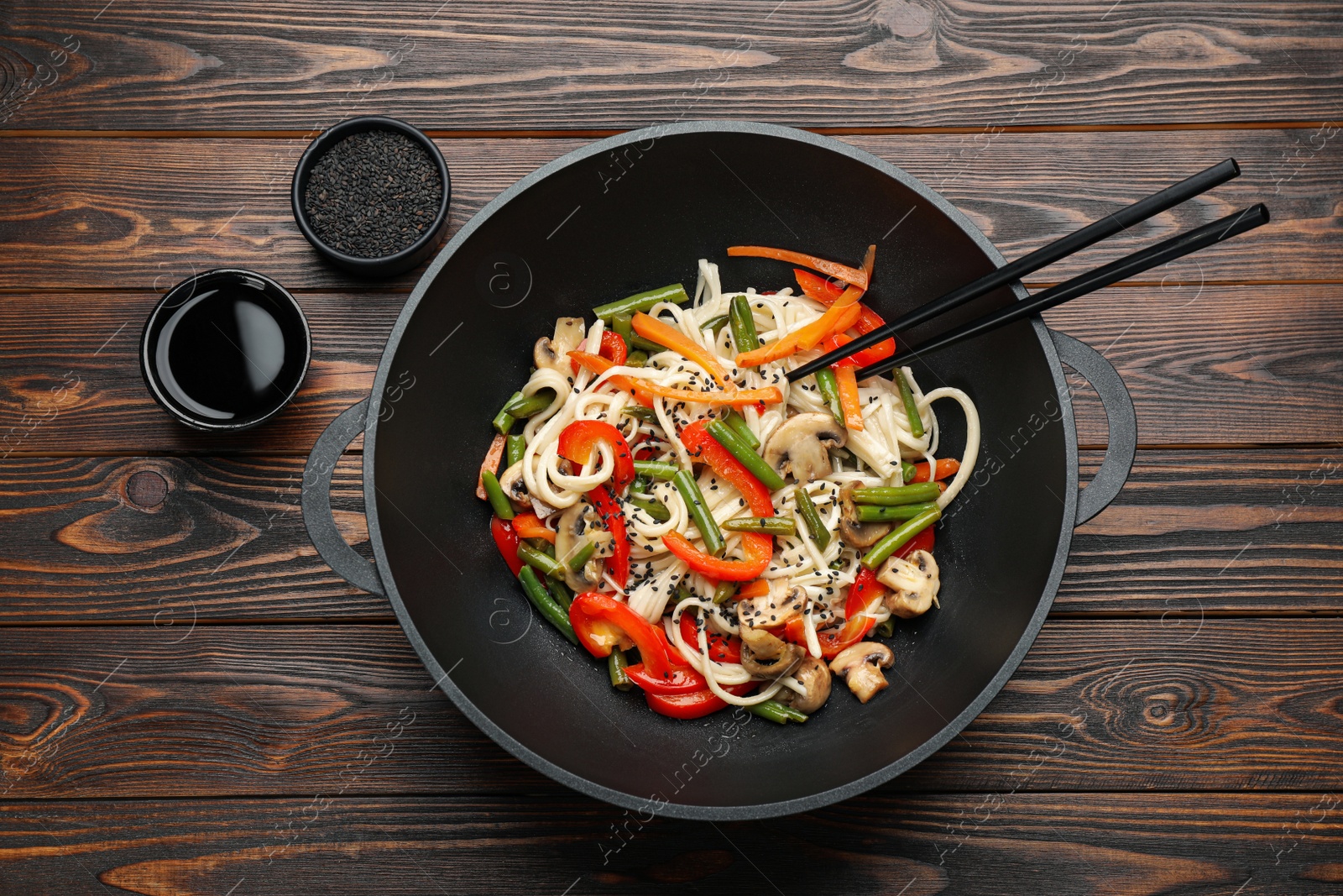 Photo of Stir fried noodles with mushrooms and vegetables in wok on wooden table, flat lay