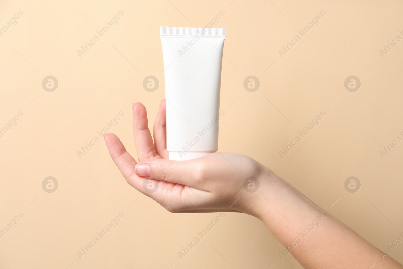 Photo of Woman with tube of hand cream on beige background, closeup