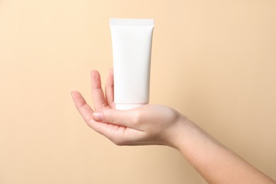 Photo of Woman with tube of hand cream on beige background, closeup