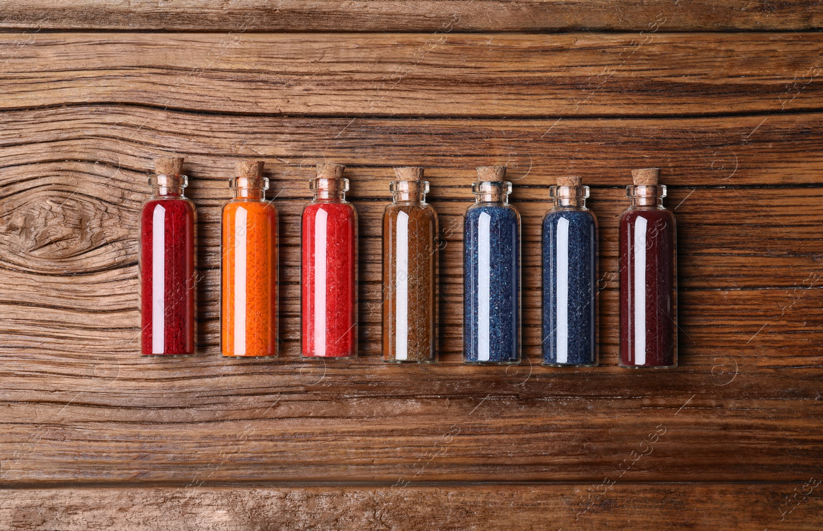 Photo of Glass bottles with different food coloring on wooden table, flat lay