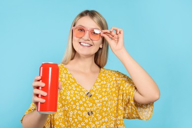 Beautiful happy woman holding red beverage can on light blue background