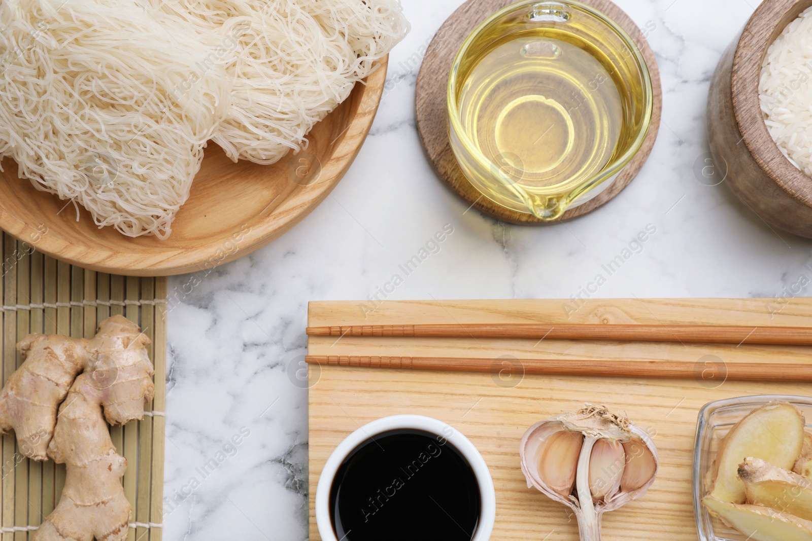 Photo of Flat lay composition with uncooked rice noodles, soy sauce and chopsticks on white marble table