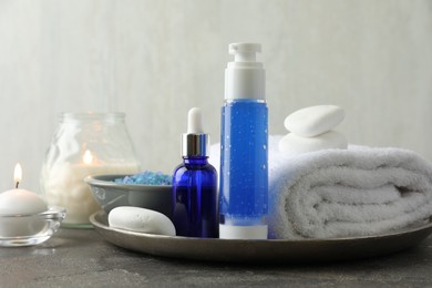 Spa composition. Cosmetic products, terry towel, burning candles and sea salt on gray table against light background