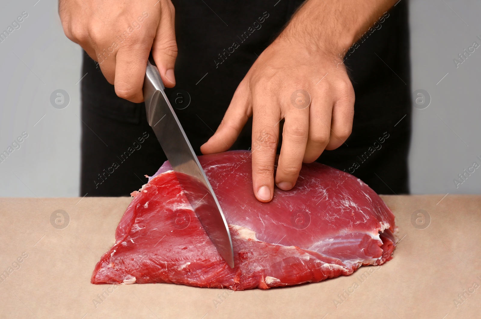 Photo of Butcher cutting fresh raw meat on counter in shop, closeup