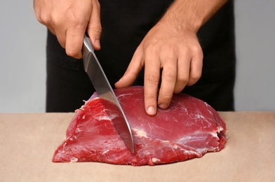 Butcher cutting fresh raw meat on counter in shop, closeup