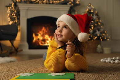 Cute child writing letter to Santa Claus while lying on floor at home. Christmas celebration