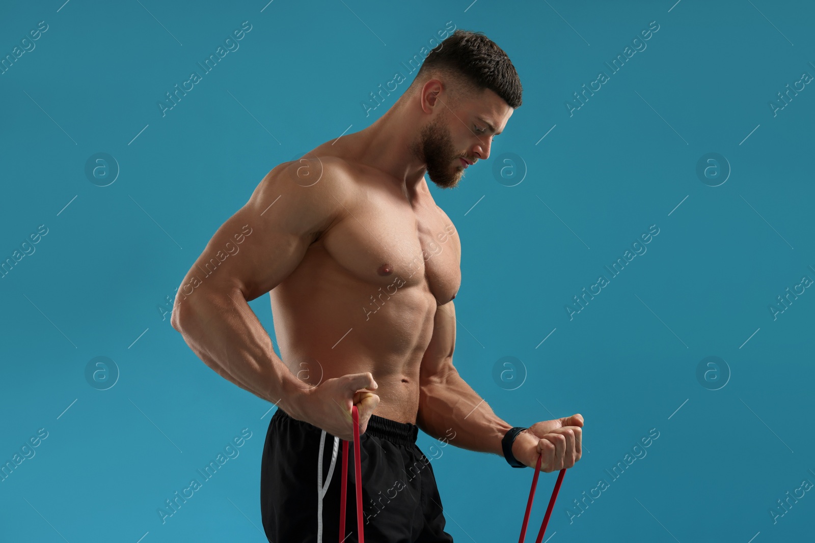 Photo of Muscular man exercising with elastic resistance band on light blue background