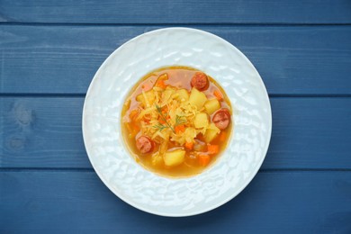 Photo of Delicious sauerkraut soup with smoked sausages and carrot on blue wooden table, top view
