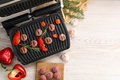 Photo of Electric grill with vegetables, meat balls and rosemary on wooden table, flat lay. Space for text