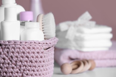 Photo of Baby cosmetic products and hair brush in knitted basket on white table, closeup. Space for text