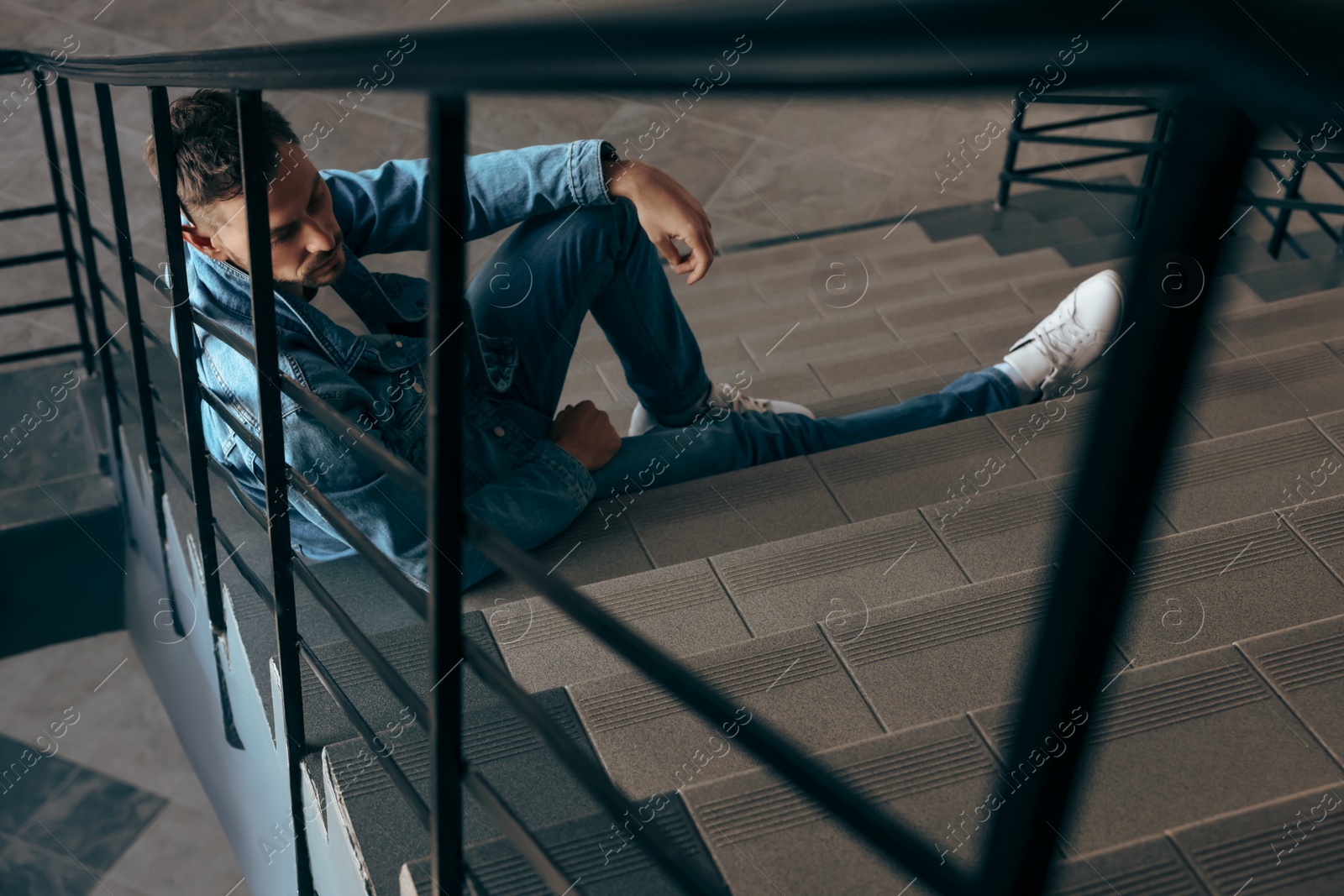 Photo of Upset man sitting on stairs indoors. Loneliness concept