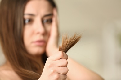 Emotional woman with damaged hair on blurred background, selective focus. Split ends
