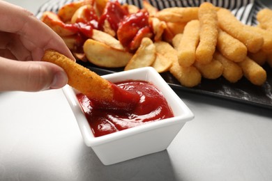 Woman dipping delicious cheese stick into bowl with ketchup on light grey table, closeup