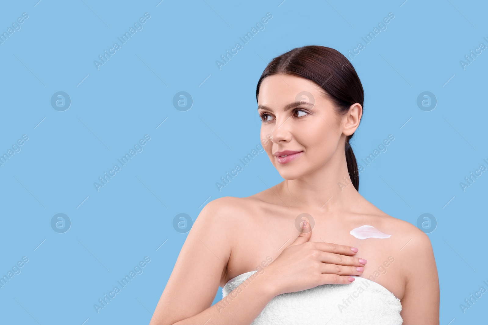 Photo of Beautiful woman with smear of body cream on light blue background, space for text