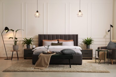 Stylish bedroom interior with large comfortable bed, armchair and ottoman