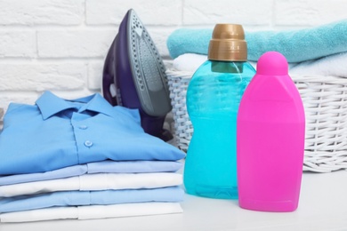 Stack of clean clothes, iron, detergents and basket with towels on table