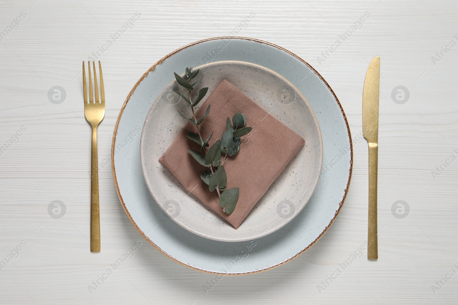 Photo of Stylish setting with cutlery and eucalyptus leaves on white wooden table, flat lay