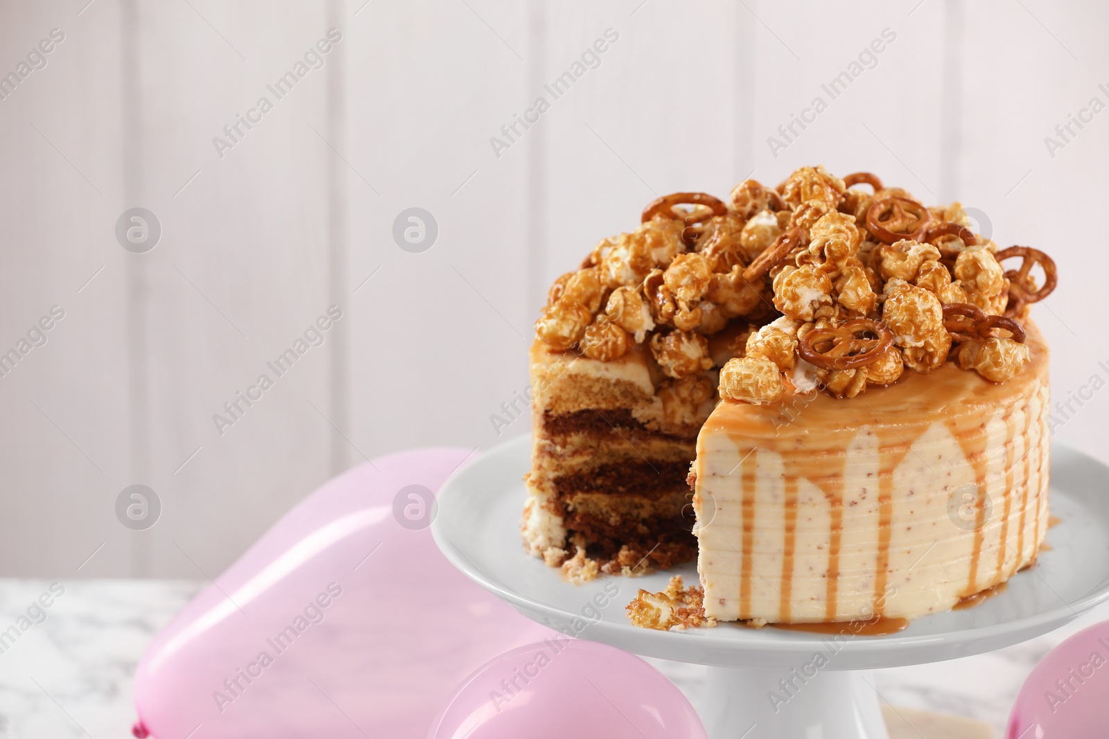 Photo of Caramel drip cake decorated with popcorn and pretzels on table, closeup. Space for text