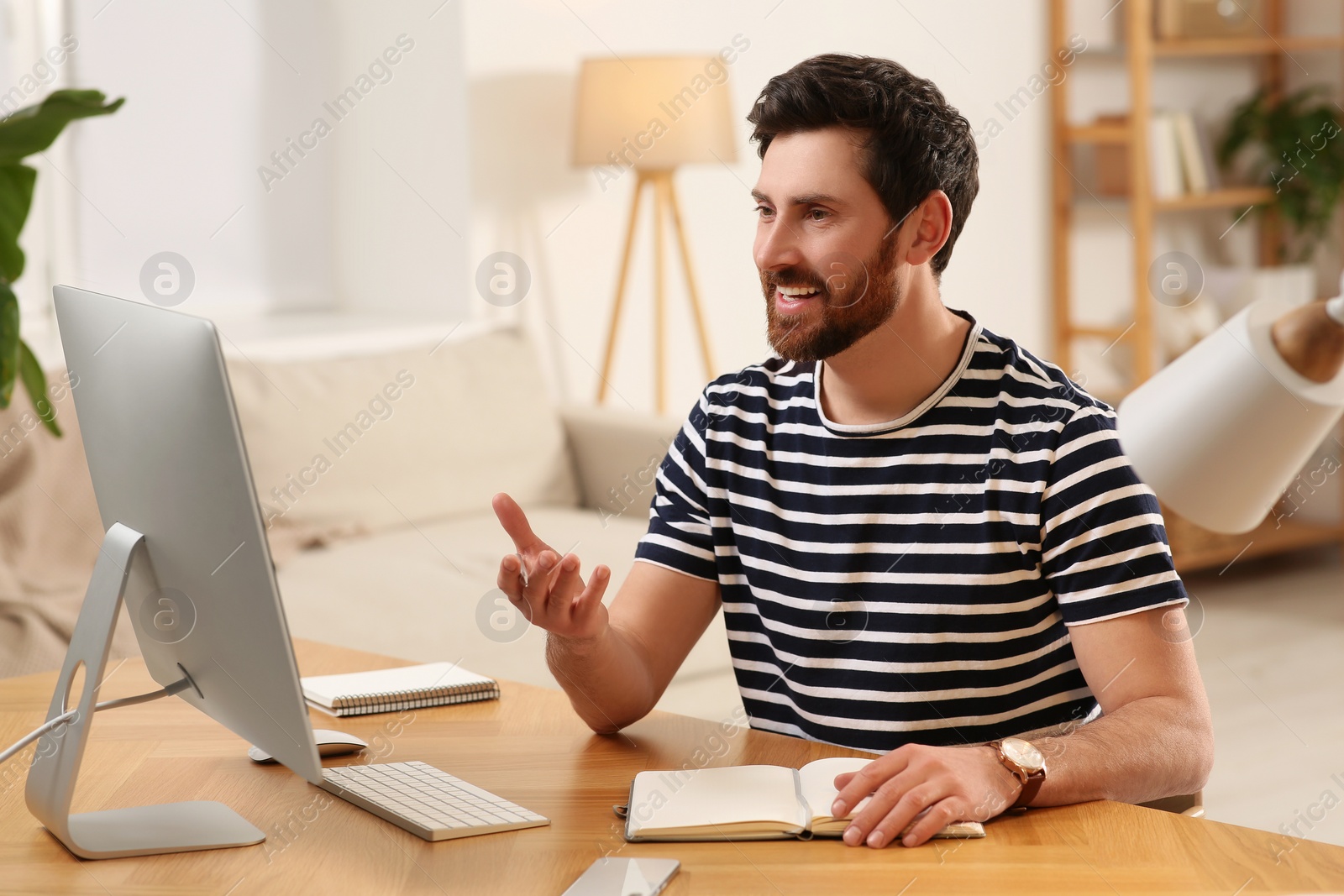 Photo of Home workplace. Happy man having video conference at wooden desk in room