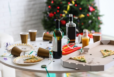 Photo of Messy table with cups, bottles and pizza indoors. Chaos after party