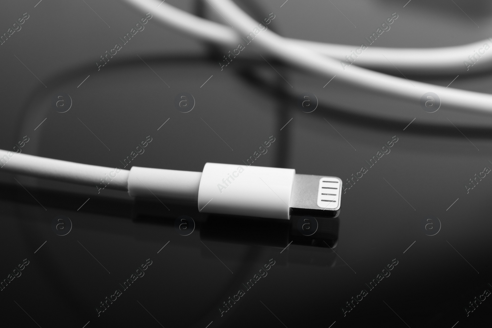 Photo of Charge cable on black reflective surface, closeup. Modern technology