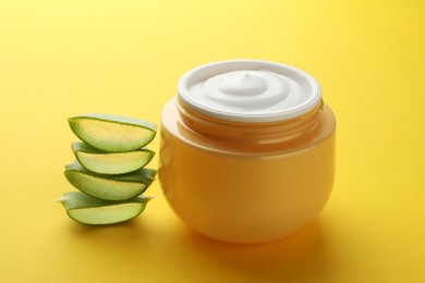 Photo of Jar with cream and cut aloe leaf on yellow background, closeup