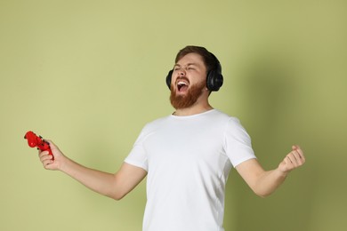 Emotional man with game controller on pale green background