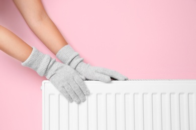 Woman in gloves warming hands on heating radiator near color wall