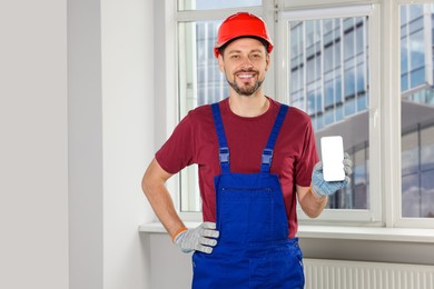 Professional repairman in uniform with phone indoors, space for text