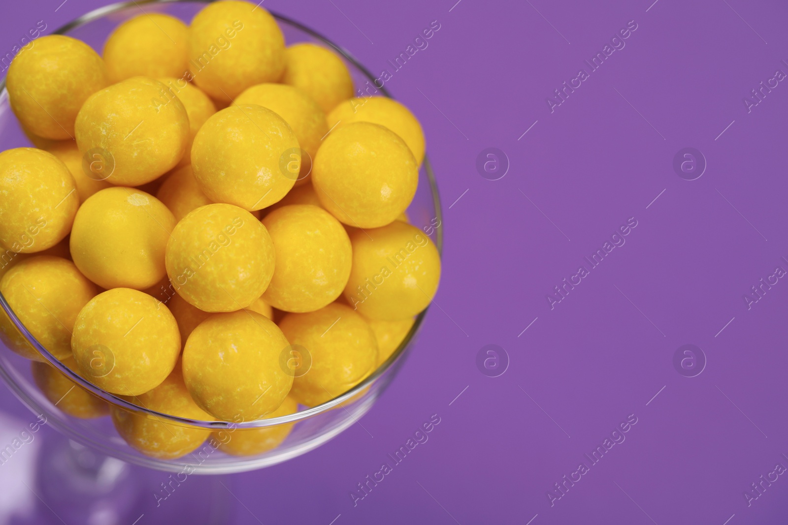 Photo of Tasty lemon chewing gums in glass on purple background, closeup. Space for text