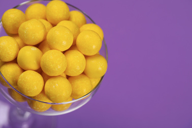 Photo of Tasty lemon chewing gums in glass on purple background, closeup. Space for text