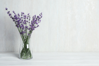 Photo of Beautiful lavender flowers in glass vase on white wooden table against light background. Space for text