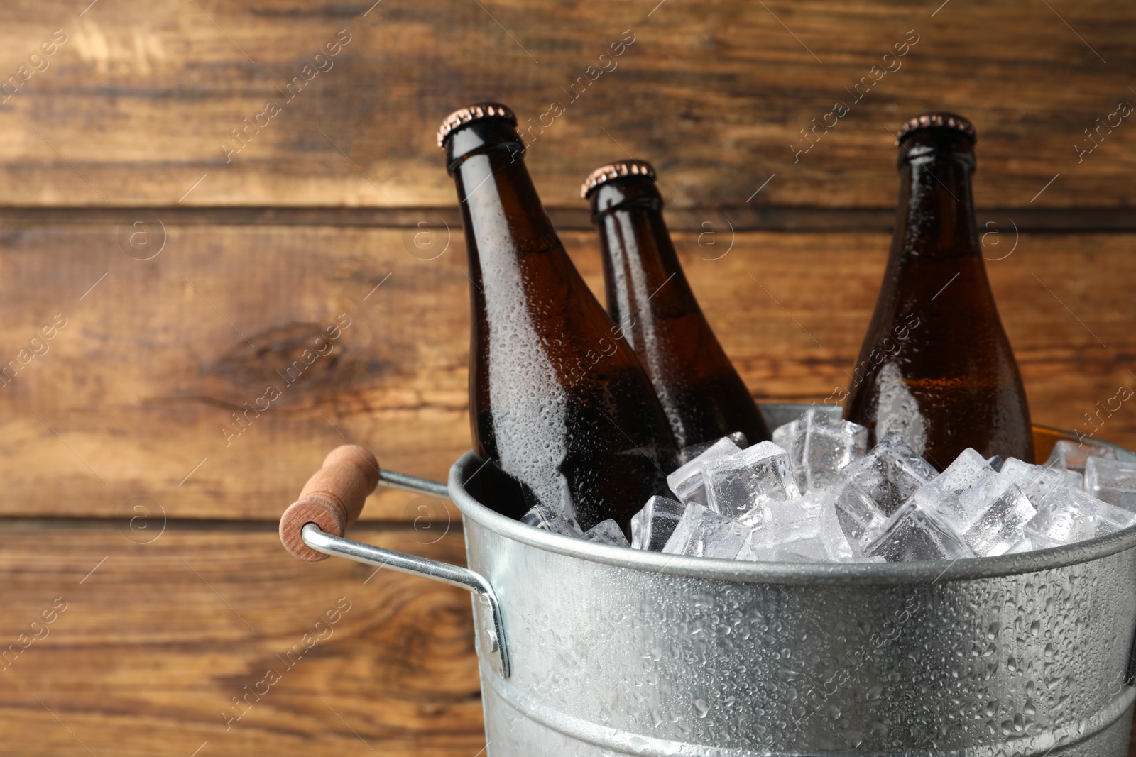 Photo of Metal bucket with beer and ice cubes on wooden background