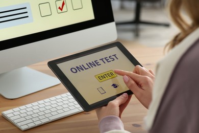 Photo of Woman taking online test on tablet at desk indoors, closeup