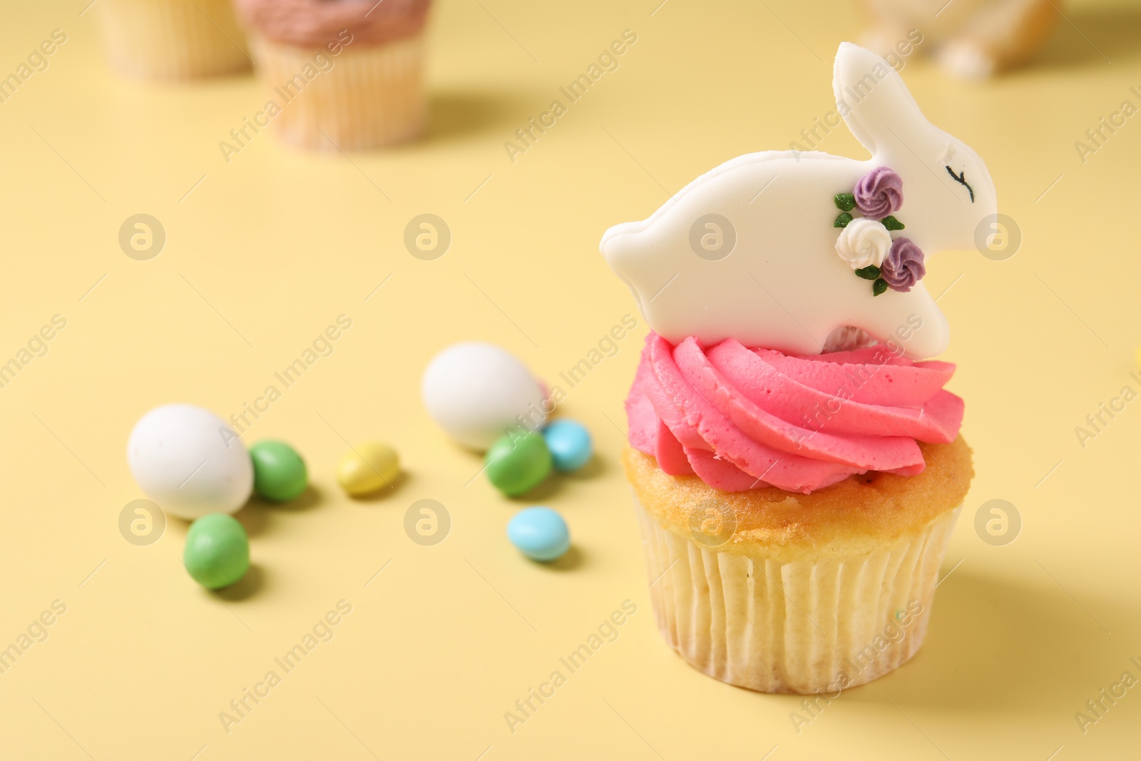 Photo of Tasty cupcake with Easter decor on pale yellow background, closeup